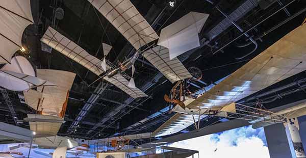 Several beige biplanes hang from the ceiling over exhibitry.